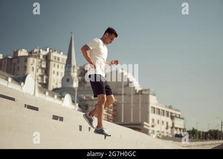 Seitenansicht des athletischen Mannes, der im Sommer am sonnigen Tag in der Stadt unten läuft Stockfoto
