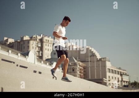 Seitenansicht des athletischen Mannes, der im Sommer am sonnigen Tag in der Stadt unten läuft Stockfoto