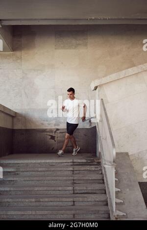 Passen Sie den männlichen Läufer in die Sportkleidung, die im Sommer während des aktiven Trainings in der Stadt unten läuft Stockfoto