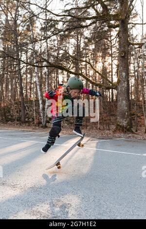 Energisches Teenager-Mädchen in Schutzausrüstung springen über dem Boden mit Skateboard und Durchführung Trick Stockfoto