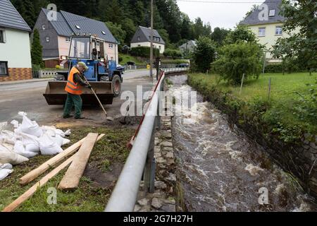 13. Juli 2021, Sachsen, Jöhstadt: Im Erzgebirgskreis Steinbach im Landkreis Jöhstadt im Erzgebirgskreis laufen Sanierarbeiten nach einem Sturzflut. Am Tag nach dem Hochwasser sind Bewohner, Bauhof, Feuerwehr und Hilfskräfte mit den Reinigungsarbeiten beschäftigt. Ankommende Fremdkörper blockieren die Abflüsse ständig. Einer der Bewohner von Jöhstädt wurde von der Sturzflut mitgerissen, er ist immer noch vermisst. Foto: Ronny Küttner/dpa Stockfoto