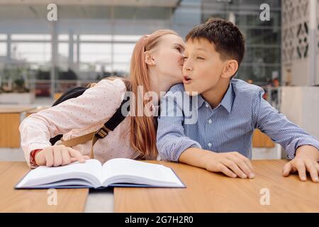 Das Mädchen im Teenageralter flüstert etwas ins Ohr des Jungen oder küsst ihn. Stockfoto