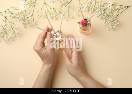 Weibliche Hände, Diffusoren und Blumen auf beigem Hintergrund Stockfoto
