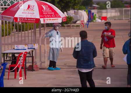 Phnom Penh, Kambodscha. 14. Juli 2021. Seit fast 5 Monaten kämpft Phnom Penh gegen einen COVID - 19-Anstieg. Ein EMT/Sanitäter in voller PSA leitet eine Massenteststelle, während ein kambodschanischer Mann mit einer Flasche Händedesinfektionsmittel/Desinfektionsmittel auskommt. Quelle: Kraig lieb / Alamy Live News Stockfoto