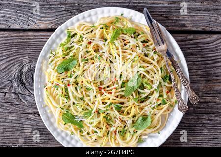 Sommer-Spaghetti alla carrettiera mit Minzblättern, Zitronenschale, Pecorino-Käse, Chilischoten-Flocken, Petersilie und geriebenen Zucchini auf einem weißen Teller Stockfoto