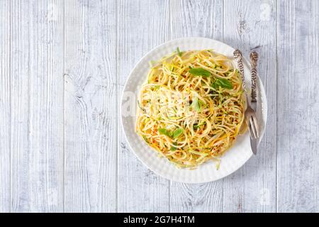 Sommer-Spaghetti alla carrettiera mit Minzblättern, Zitronenschale, Pecorino-Käse, Chilischoten-Flocken, Petersilie und geriebenen Zucchini auf einem weißen Teller Stockfoto