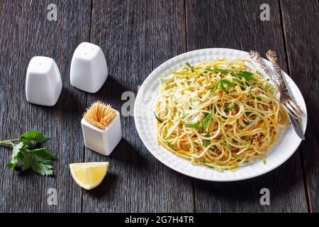 Sommer-Spaghetti alla carrettiera mit Minzblättern, Zitronenschale, Pecorino-Käse, Chilischoten-Flocken, Petersilie und geriebenen Zucchini auf einem weißen Teller Stockfoto