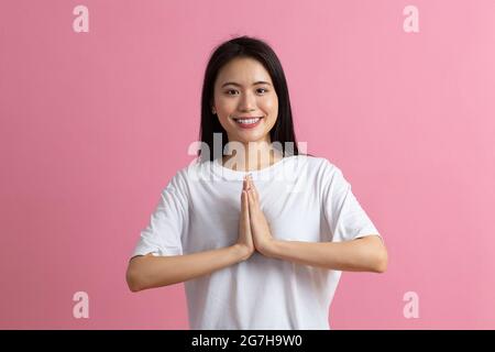 Namaste Porträt einer asiatischen Frau, die die Handflächen zusammenhält und sich vor rosa Hintergrund in einer asiatischen Grußgeste verbeugt Stockfoto