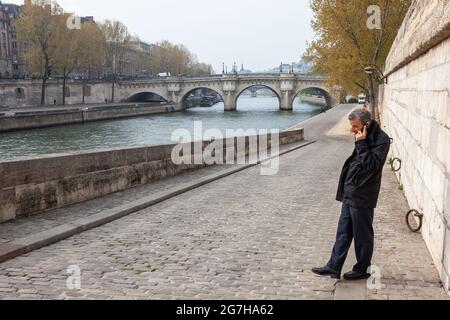 Mann telefonieren auf einem Kai der seine, die Pont Neuf im Hintergrund. Paris, Frankreich Stockfoto