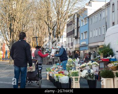 Neuwied, Deutschland - 26. März 2021: Ein Marktstand mit einer Vielzahl von Blumen auf einem Bauernmarkt mit Kunden und Verkäufer mit Gesichtsmasken durch Co Stockfoto