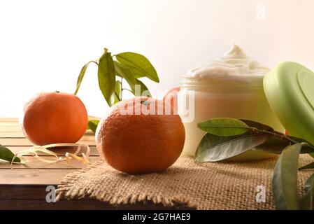 Natürliche Hautcreme mit Mandarinenextrakt mit Früchten und Blättern auf Holztisch. Vorderansicht. Stockfoto