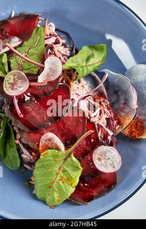 Brosaola, dünn geschnitten mit Salat italiana gesalzenem Rindfleisch auf einem Teller mit Sauce und Rote Bete Blätter close-up. Stockfoto