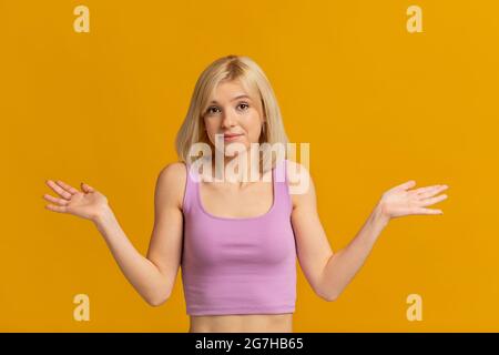 Wer weiß. Porträt einer jungen, rätselhaften Dame, die mit den Schultern zuckt und die Kamera anschaut, auf gelbem Hintergrund posiert, Studioaufnahme. Tut mir leid, exuse me, Stockfoto