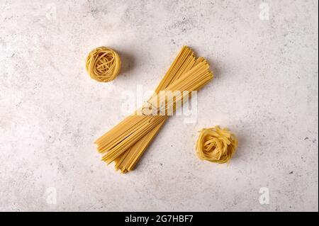 Ungekochte, rohe Gruppe von Spaghetti, Fettuccine und Tagliatelle auf grauem texturiertem Hintergrund. Speicherplatz kopieren. Draufsicht Stockfoto