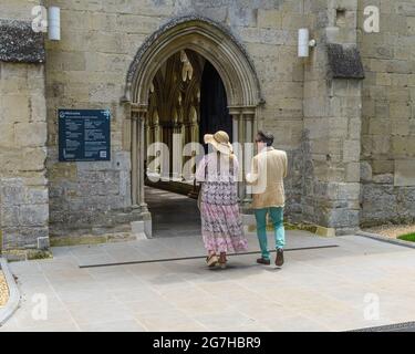 Salisbury, Wiltshire, Großbritannien, 14. Juli 2021, Wetter: Ein warmer Sommertag auf dem Gelände der Salisbury Cathedral mit Temperaturen bis in die Mitte der 20er Jahre und steigenden Temperaturen, wenn sich eine Hitzewelle aus dem Süden bildet. Ein besuchtes Paar betreten das Tor zu den Kreuzgängen, von wo aus der Eingang zum Hauptknave gemacht werden kann. Kredit: Paul Biggins/Alamy Live Nachrichten Stockfoto