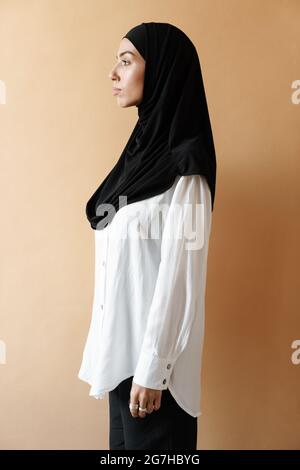 Eine Seitenansicht der muslimischen Frau im Hijab, die im orangen Studio steht Stockfoto
