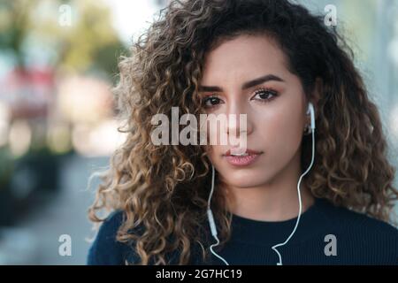 Junge lateinerin, die im Freien mit Ohrhörern steht. Stockfoto