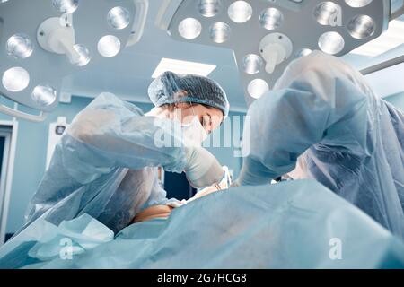 Chirurgen Männer und Frauen in einem Team während einer Operation über dem Operationstisch führen Ärzte in modernen Geräten eine onkologische Operation durch. Stockfoto