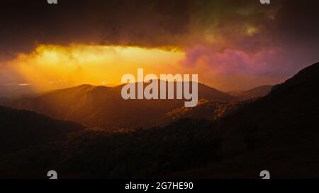 Dramatischer Regensturm versteckt die untergehende Sonne und den Bergrücken, magischer Scheinwerfer leuchtet durch dunkle Wolken auf die Berge. Konzentrieren Sie sich auf Berge. Stockfoto