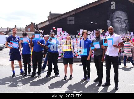 Schüler und andere von der Castlefield School, Manchester, posieren mit Aussagen, die sie erstellt und zum Verlassen des Wandbildes gebracht haben. Auf dem riesigen Marcus Rashford Wandgemälde in Withington, Manchester, England, Großbritannien, hinterlassen Menschen Blumen und Hunderte unterstützender Notizen, Bilder, Flaggen und antirassistische Botschaften, die nach dem Verlust der englischen Fußball-Europameisterschaft 2020 am 11. Juli 2021 mit missbräuchlichen Graffiti verwüstet wurden. Das Wandbild wurde von dem in Frankreich geborenen Straßenkünstler Akse P19 an der Wand des Coffee House Cafe in der Copson Street geschaffen. Stockfoto