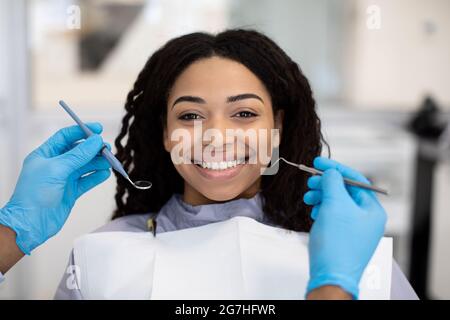 Porträt der lächelnden afroamerikanischen Lady bekommen Zähne Behandlung in der Zahnklinik, Happy Young Black weibliche Patientin mit Check-up mit Zahnarzt in M Stockfoto