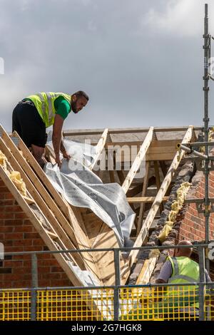Keepmoat beherbergt Immobilienentwickler, eine Baustelle in Chorley. Bauarbeiter beginnen mit dem Bau dieses großen neuen Wohngebiets. Klober Permo Air Open Underlay Dachbelag Dachpappe, Dächer Holzleisten Dormer, Dachretter und Dachinnenbau, Dachträger, Wangenfassade Holzbretter Soffitrahmen und Verkleidungen Dachhölzer. Ein Schlafsaal mit Schrägdach, das auf einem grünen Ackergrundstück errichtet wurde. Stockfoto