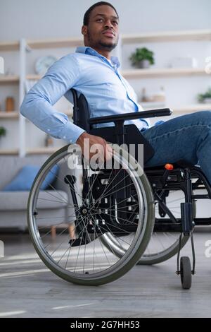 Trauriger, behinderter junger Mann im Rollstuhl, der sich zu Hause allein und deprimiert fühlt, Blick aus der Ferne. Unglücklicher schwarzer Kerl mit körperlicher Beeinträchtigung, der emotional ist Stockfoto
