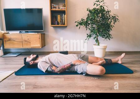 Bärtiger Mann meditiert zu Hause in der Haltung der Windlinderung Stockfoto