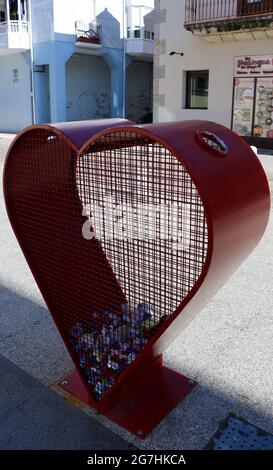 Herzförmiger roter Recyclingbehälter für Kunststoffkappen in einer Straße in Santona Cantabria, Spanien Stockfoto