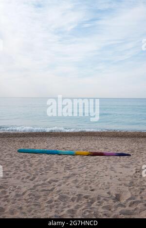 Ein Stück Treibholz, das in mehreren Farben gestrichen wurde, liegt verlassen an einem Strand mit einem ruhigen mittelmeer im Hintergrund Stockfoto