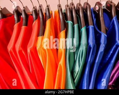 Regenbogenfarben. Wahl der lässigen Kleidung auf schwarzen Kleiderbügeln, isoliert auf weiß.Vielzahl von Seidenkleider auf Kleiderbügeln.Bunte Kleidung im Kleiderschrank hängen Stockfoto
