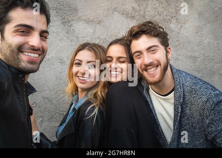 Porträt von Millennials, die die Kamera anlächeln. Eine Gruppe junger Leute, die sich gemeinsam an einer Betonwand amüsieren. Stockfoto