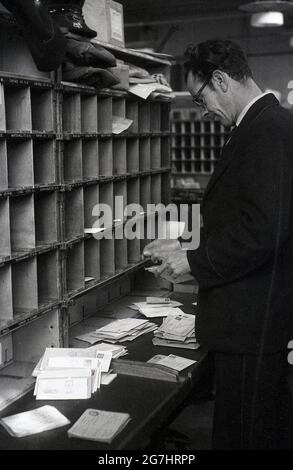 In den 1950er Jahren, historisch, ein männlicher GPO-Arbeiter, der Briefe oder Post in die Kubbylöcher für die Straßen des Bezirks, London, England, Großbritannien, aussortierte. Stockfoto