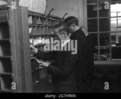 In den 1950er Jahren sortierte drei männliche GPO-Arbeiter Briefe oder Post in den Kubby oder Taubenlöcher auf einem Regal, das in die Dfferent Streets des Bezirks, London, England, Großbritannien, aufgeteilt war. Stockfoto