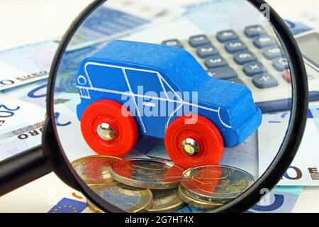 Eine Lupe konzentriert sich auf das Auto, das Geld und den Rechner. Eine Metapher für die Autofinanzierung. Stockfoto