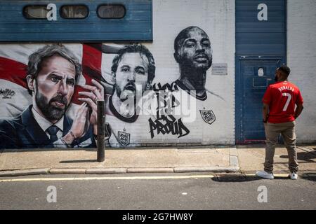 London, Großbritannien. 14. Juli 2021. Ein Mann, der ein Cristiano Ronaldo-Hemd trägt, sieht ein Wandgemälde der städtischen Straßenkünstler MurWalls, das von Sadiq Khan, dem Bürgermeister von London, in Vinegar Yard in der Nähe der London Bridge enthüllt wurde. Mit dem Slogan „You did US proud“ feiert das Kunstwerk die Erfolge der englischen Fußballmannschaft beim Erreichen des Finales der Euro 2020 und zeigt ein Bild von Manager Gareth Southgate, Kapitän Harry Kane und dem Stürmer Raheem Sterling. Kredit: Stephen Chung / Alamy Live Nachrichten Stockfoto