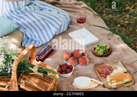 Kurzer Blick auf leckeres Essen und Wein in der Nähe von Korb und Frau auf der Decke im Park Stockfoto