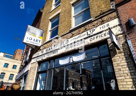 Ein altes Ladenschild für W Wakefield Spitalfields an einer Fassade, Commercial Street, Spitalfields, London, Großbritannien Stockfoto