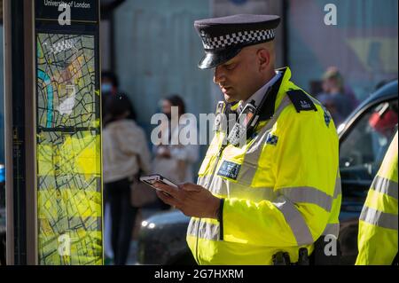 LONDON - 29. MAI 2021: Britischer Polizist in einer gut sichtbaren Jacke schaut auf ein Mobiltelefon Stockfoto