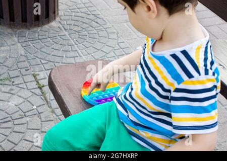 Ein Kind von 4 Jahren spielt mit Pop IT im Stadtpark. Anti-Stress-Spielzeug für die Entwicklung von Feinmotorik bei Kindern. Stockfoto