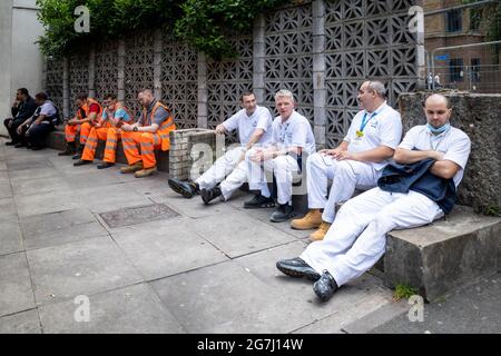 London, Großbritannien. 14. Juli 2021. Krankenhauspersonal und Bauarbeiter in der Nähe von Guy’s und St. Thomas' Hospital machen bei dem aktuell warmen Wetter eine Pause im Freien. Angesichts der Lockung der Blockierung am 19. Juli prognostiziert die Wissenschaftler einen signifikanten Anstieg der Zahl der positiven Coronavirus-Fälle. Kredit: Stephen Chung / Alamy Live Nachrichten Stockfoto