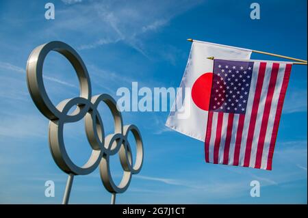 RIO DE JANEIRO - MÄRZ 2016: Flaggen der USA und Japans hängen vor einem großen Satz glänzender metallischer olympischer Ringe unter hellblauem Himmel zusammen. Stockfoto