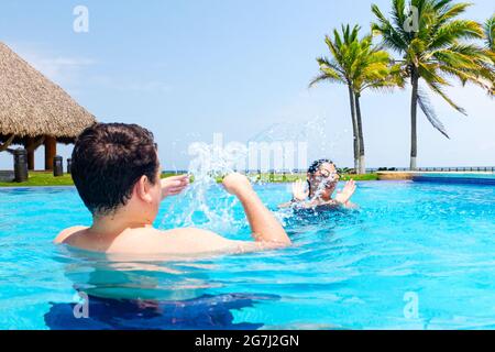 Glücklicher Freund und Freundin oder Mann und Frau, die im Pool spielen und Wasser spritzen Stockfoto