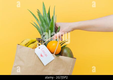Frau Hand hält Papiertüte voller tropischer Früchte auf gelbem Hintergrund. Speicherplatz kopieren. Stockfoto