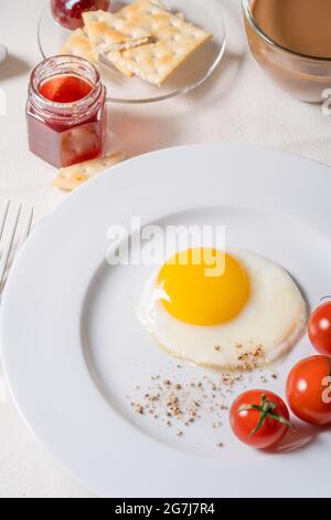 Esstisch zum Frühstück. Kaffee, Milch, Spiegelei, Kirschtomaten, Obstkonfitüre auf Leinentischdecke Stockfoto