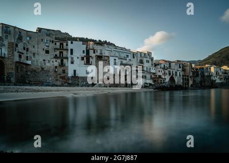 Sonnenaufgang im Hafen von Cefalu, Sizilien, Italien, Altstadt Panoramablick mit bunten Häusern am Wasser, Meer und La Rocca Klippe.Attraktive Sommer-Cityscap Stockfoto