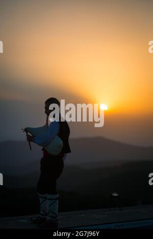 Ein junger Dudelsackläufer in Volkstracht spielt auf einem Berggipfel, wenn die Sonne aufgeht, am 01. Juli 2021, Shipka, Bulgarien Stockfoto