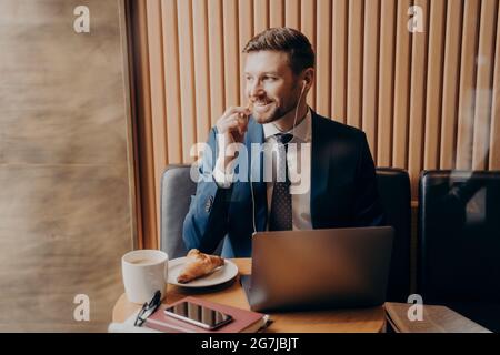 Männlicher Investor in blauem Anzug, der online mit einem Geschäftspartner über einen Laptop im Restaurant spricht Stockfoto