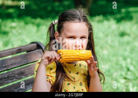 Familienwochenende im Park an einem sonnigen Tag isst das Kind leckeren süßen Mais Stockfoto