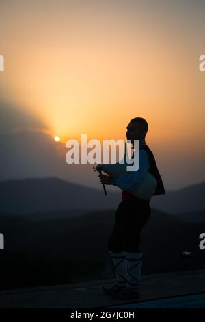 Ein junger Dudelsackläufer in Volkstracht spielt auf einem Berggipfel, wenn die Sonne aufgeht, am 01. Juli 2021, Shipka, Bulgarien Stockfoto